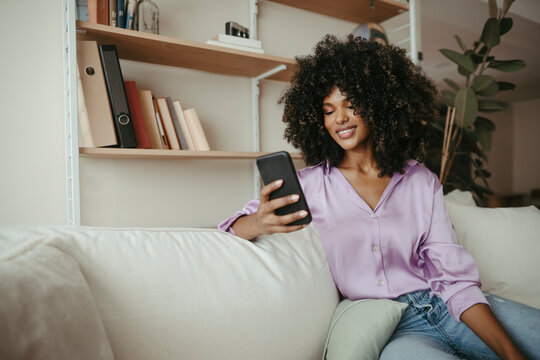 Young woman with Afro hairstyle using mobile phone in living room