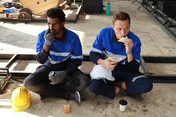 Happy teamwork technician engineer in safety workwear having lunch and eating sandwich and coffee at industry manufacturing factory