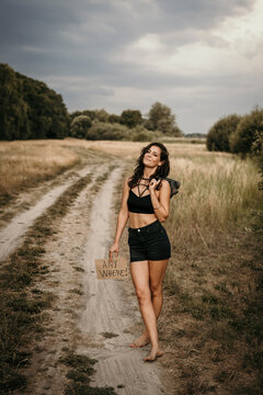 Woman with anywhere text on cardboard standing on dirt road