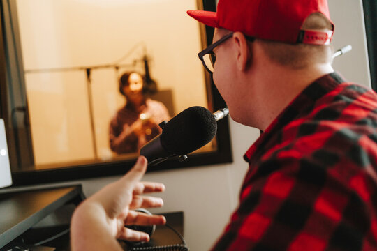 Musician talking with singer through microphone at studio