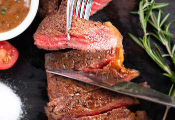 Grilled sliced Strip Loin Beef Steak with tomatoes mushroom and rosemary on a dark wooden. 