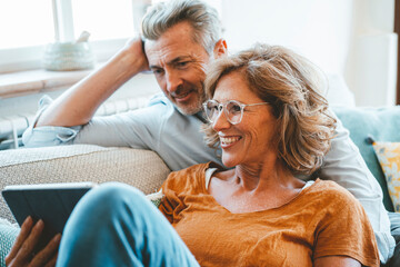 Happy mature woman wearing eyeglasses using tablet PC by man at home
