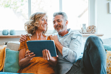 Happy mature couple sitting with tablet computer on sofa at home