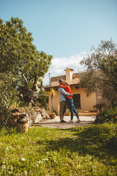 Mature woman embracing man standing in front of house on sunny day