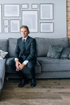 Confident mature businessman wearing suit sitting on sofa at home