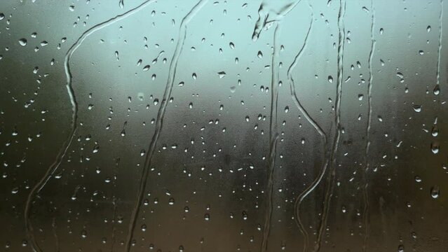raindrops sliding fast down a window pane with the background out of focus 