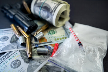 Packages of powdered substances and dollar bills next to a gun and a medical syringe.
