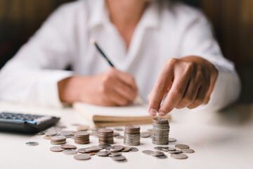 Businessman holding coins putting on stacking coins and taking notes. plan revenue and expenses, target success growth, finance profit planning 2023 concept.