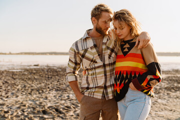 Happy young white couple hugging and walking by seashore