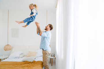 Young father throwing his little daughter in air and having fun at home