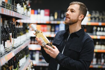Portrait of young glad positive male customer selecting wine in supermarket
