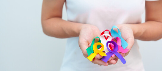 World cancer day, February 4. Hand holding blue, red, teal, white, pink, purple and yellow ribbons...