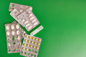 Packages with various pills and a container with liquid on a green background.