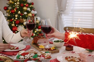 Family with sparklers clinking glasses at festive dinner indoors, closeup. Christmas Eve celebration