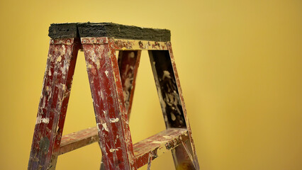 Old used construction painter ladder with painted splatter standing in front of the yellow wall...