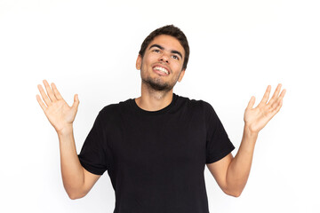 Naklejka premium Careless young man shrugging. Portrait of cheerful Caucasian male model with short dark hair in black T-shirt looking away with raised arms, showing helpless gesture. Confusion concept