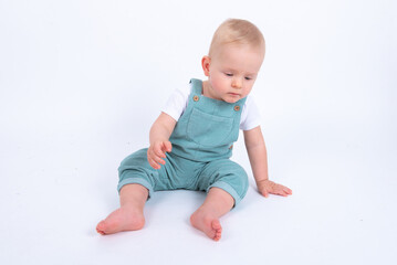 Close-up portrait of beautiful baby boy wearing light blue jumpsuit over white studio background...