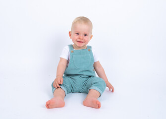 Close-up portrait of beautiful baby boy wearing light blue jumpsuit over white studio background smiling and looking to the camera. 