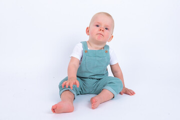 Close-up portrait of beautiful baby boy wearing light blue jumpsuit over white studio background...