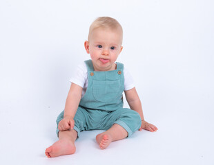 Portrait of beautiful baby boy wearing light blue jumpsuit over white studio background showing his tongue, smiling and looking to the camera. 