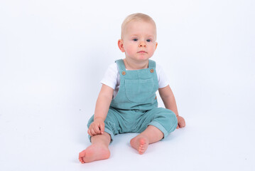 Portrait of beautiful baby boy wearing light blue jumpsuit over white studio background smiling and looking to the camera. 