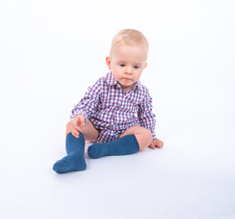 Playful beautiful baby boy wearing plaid bodysuit standing over white studio background sitting and smiling to the camera. Baby boy wants to play with his mother 