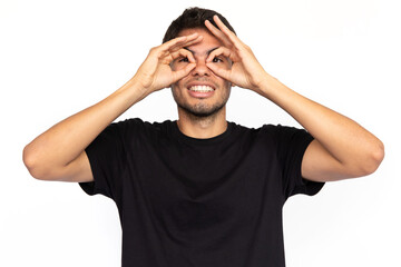 Excited young man doing glasses gesture. Happy Caucasian male model with short dark hair in black T-shirt looking at camera, smiling with ok signs. Entertainment, grimacing concept