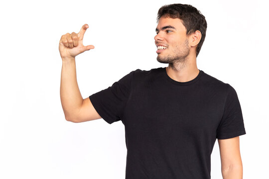 Happy Young Man Holding Invisible Object. Excited Caucasian Male Model With Short Dark Hair In Black T-shirt Looking Away, Smiling While Showing Something Small. Advertisement, Size Concept