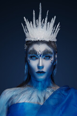 Snow queen with painted skin and make up dressed in blue cape and ice crown.