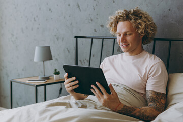 Young man wear white t-shirt pajama he lying in bed use hold tablet pc computer rest relax spend time in bedroom home in own room hotel wake up dream be in reverie good mood day. Real estate concept.