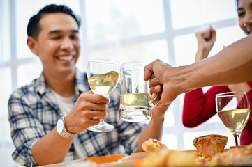 Joyful and happy Asian man clinking a glass of wine with his friend's glass of beer at the party.