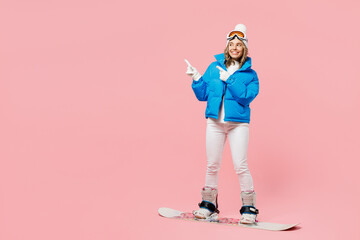Snowboarder fun woman wear blue suit goggles mask hat ski padded jacket snowboarding point finger aside isolated on plain pastel pink background. Winter extreme sport hobby weekend trip relax concept. © ViDi Studio
