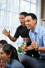 Two excited Asian male friends football fans watching football on TV at home together.