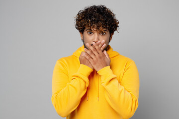 Fototapeta na wymiar Young amazed shocked scared astonished sad Indian man 20s he wears casual yellow hoody cover mouth with hand look camera isolated on plain grey background studio portrait. People lifestyle portrait.