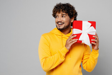 Young Indian man 20s he wearing casual yellow hoody hold in hand red present box with gift ribbon...