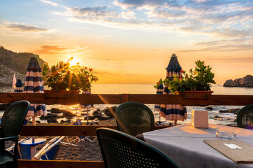 beautiful view from a restaurant terrace with tables, chairs and decoration flowers to beach and...
