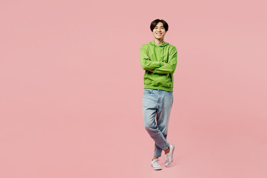 Full body smiling happy fun young man of Asian ethnicity wear green hoody look camera hold hands crossed folded isolated on plain pastel light pink background studio portrait People lifestyle concept