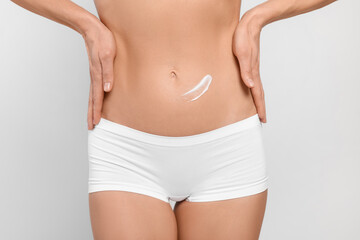 Fototapeta na wymiar Woman with body cream onto her belly against white background, closeup