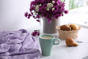 Cup of aromatic coffee, beautiful flowers and violet cloth on white table