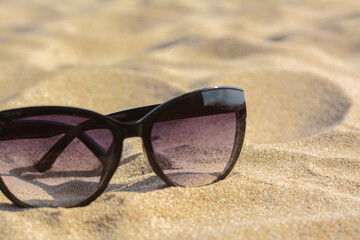Stylish sunglasses with black frame on sandy beach, closeup