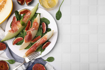 Tasty melon, jamon and figs served on white tiled table, flat lay. Space for text
