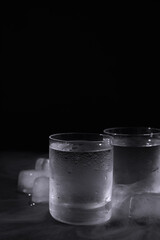 Vodka in shot glasses with ice on table against black background