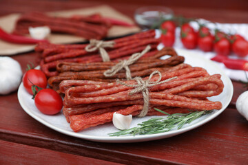 Bundles of delicious kabanosy with rosemary, garlic and tomatoes on wooden table