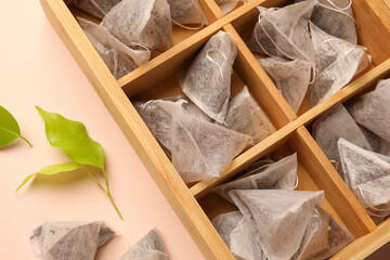 Many tea bags in wooden box and leaves on color background, closeup