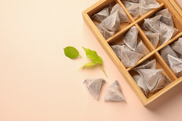 Many tea bags in wooden box and leaves on color background, flat lay. Space for text