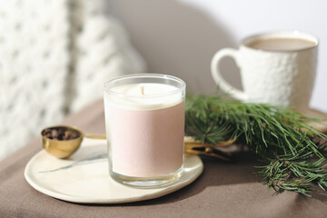 coconut wax candle in glass on a bedside table next to cup of coffee and pine branch. home scents and aromatherapy. good sleeep and relaxation