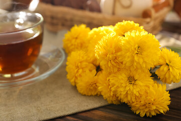 Fototapeta na wymiar Beautiful yellow chrysanthemum flowers and cup of aromatic tea on wooden table, closeup