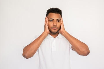 Astonished young man holding face in hands from shock. Male Indian model with brown eyes and curly hair in white polo shirt holding head with surprised facial expression. Astonishment concept