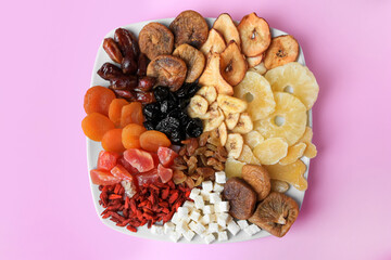 Plate with different dried fruits on violet background, top view