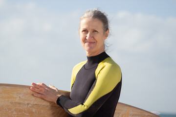 Portrait of happy senior woman enjoying surfing in sea. Smiling woman with board spending summer vacation near sea, standing and looking aside. Sport, active rest and vacation of aged people concept